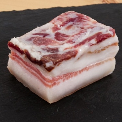 Bloco de banha de porco com camadas de gordura e carne sobre ardósia preta