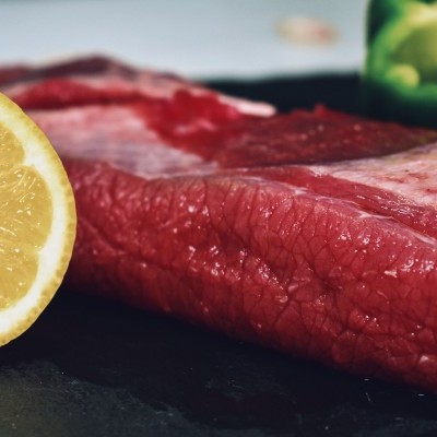 Pedaço cru de carne vermelha com metade de limão e pimento verde ao fundo