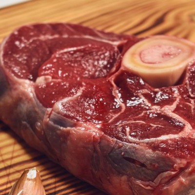 Carne crua vermelha com osso sobre tábua de madeira com alecrim e alho