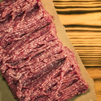 Carne picada vermelha sobre papel castanho em superfície de madeira clara