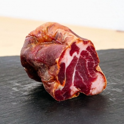 Linguiça curada castanha avermelhada com texturas marmoreadas brancas sobre tábua de ardósia preta