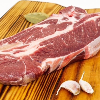 Bife cru com gordura sobre tábua de madeira com alho e folha de louro