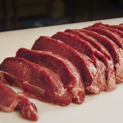 Fatias de carne vermelha crua sobre superfície branca com faca ao lado