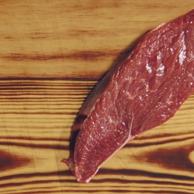 Pedaço de carne crua vermelha sobre superfície de madeira clara com veios castanhos.