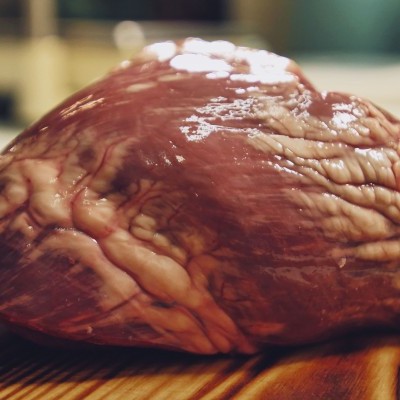 Coração cru avermelhado com veias e gordura sobre madeira listrada