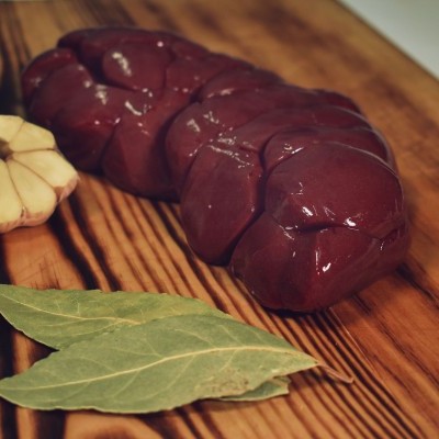 Pedaços de produto cru castanha avermelhada, alho e folhas de louro numa tábua de madeira