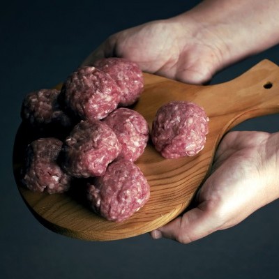 Tábua de madeira com almôndegas cruas segurada por mãos, fundo escuro