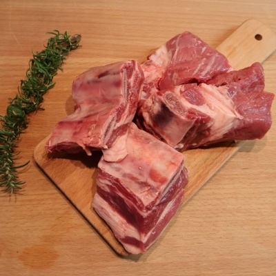Pedaços de carne com osso numa tábua de madeira e ramo de alecrim