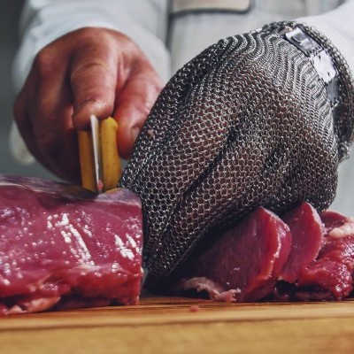 Pessoa a cortar carne vermelha com luva metálica de proteção