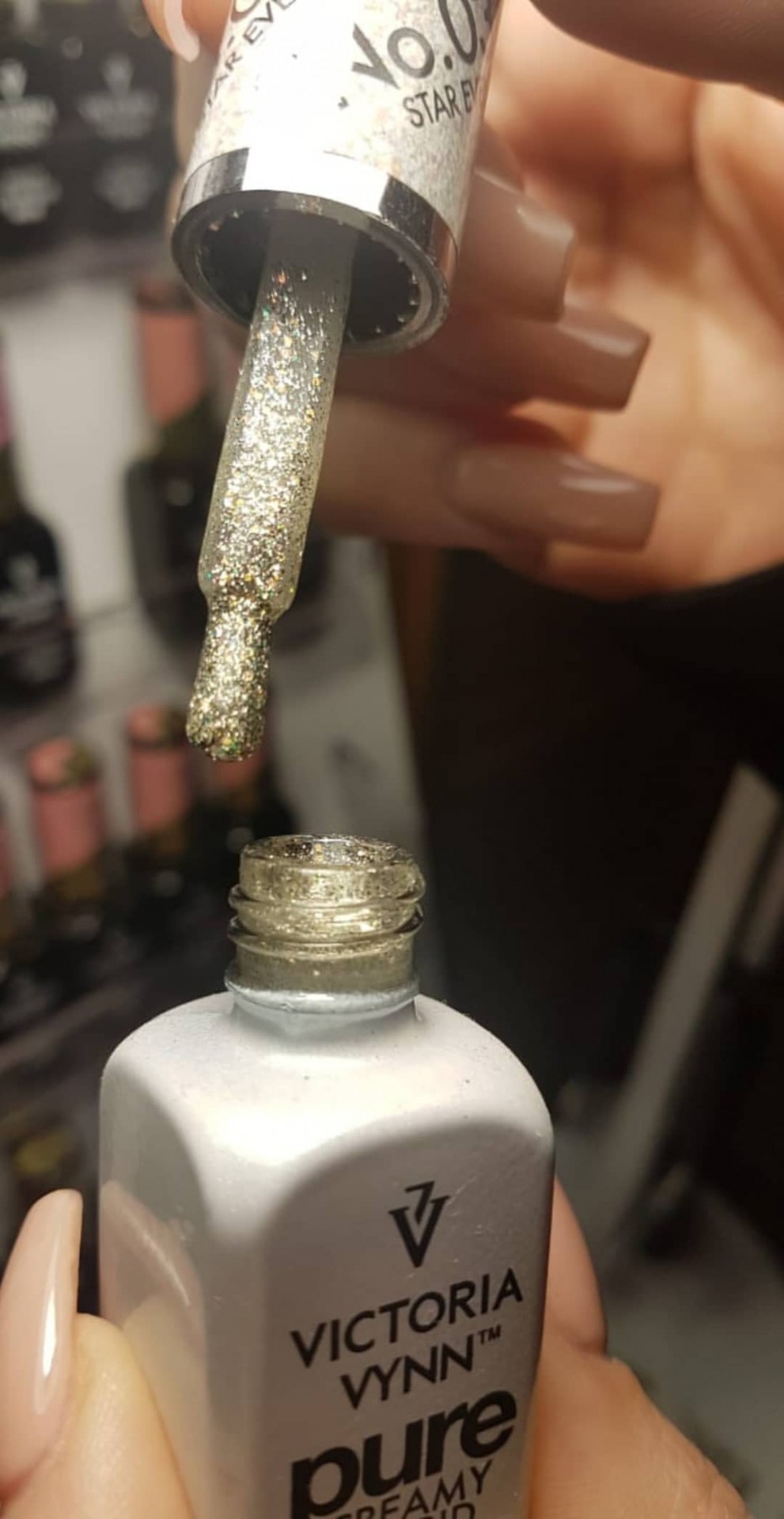 Frasco branco de verniz com pincel carregado de verniz glitter dourado e unhas com manicure nude