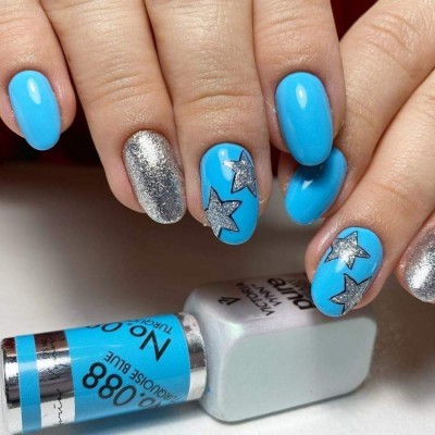 Unhas pintadas de azul turquesa e prata com estrelas prateadas e frasco de verniz no fundo