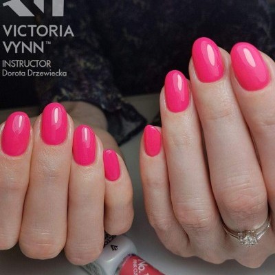 Mãos femininas com unhas cor de rosa brilhante e frasco de verniz Victoria Vynn.