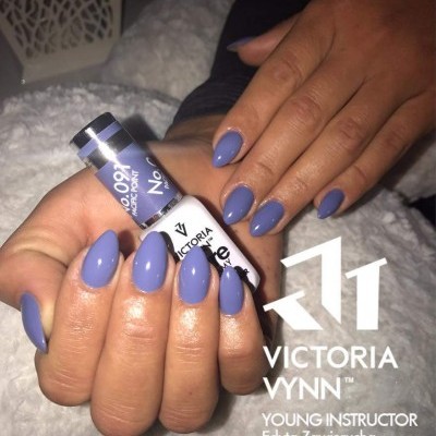 Mãos com unhas pintadas de roxo azulado segurando frasco de verniz Victoria Vynn