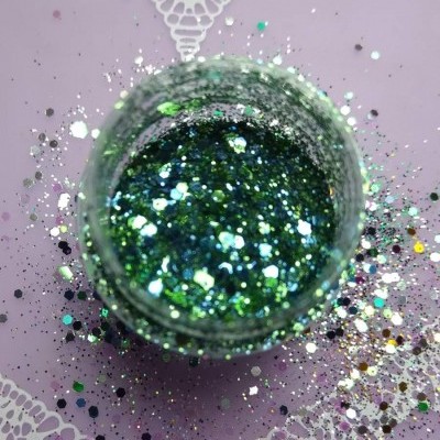 Pote pequeno aberto com glitter brilhante em verde e cores múltiplas num fundo lilás com padrão branco.