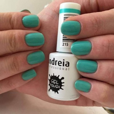 Mãos com unhas pintadas de verniz gel verde-azulado seguram frasco branco de verniz gel Andreia Professional