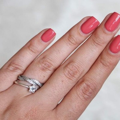 Mão com unhas coral rosa e dois anéis de prata, um com pedra em forma de estrela
