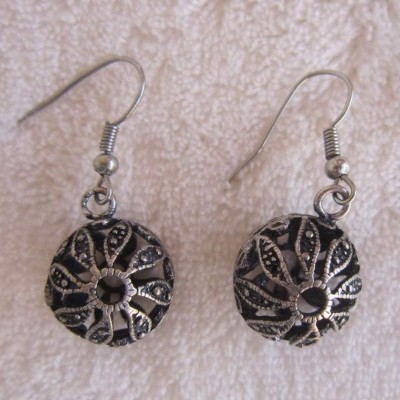 Brincos redondos em metal com padrão floral preto sobre fundo branco