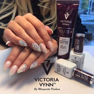 Unhas com gel nude e pedras brilhantes ao lado de produtos Victoria Vynn