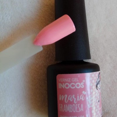 Frasco preto de verniz gel rosa com amostra na unha