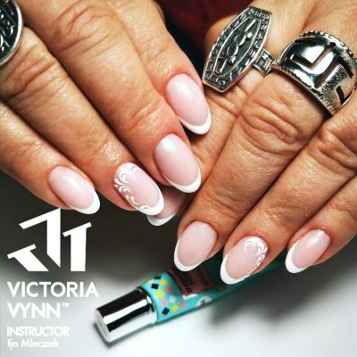 Unhas com manicure francesa e detalhes brancos, mãos com anéis prateados segurando um tubo de verniz colorido