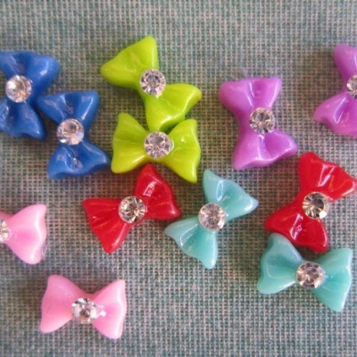 Laços coloridos de plástico com pedra brilhante no centro sobre tecido cinzento