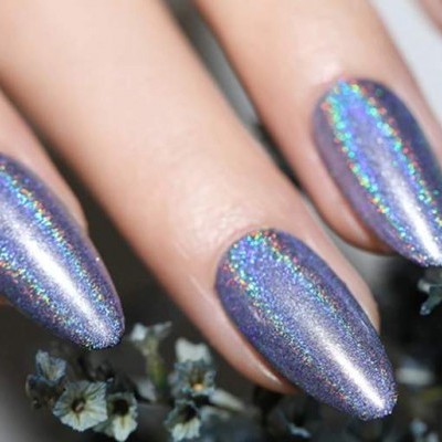 Unhas compridas com verniz holográfico prateado e flores secas ao fundo