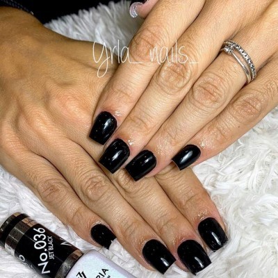 Unhas quadradas pintadas de preto brilhante com verniz próximo a dois frascos etiquetados