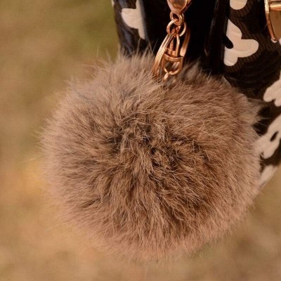 Chaveiro pompom castanho pendurado em bolsa preta com padrão branco
