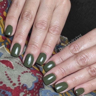 Unhas pintadas de verde fosco sobre tecido colorido com padrão floral e geométrico