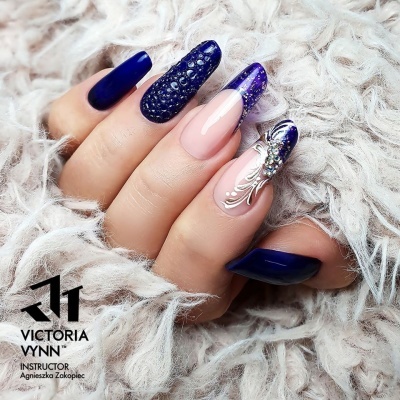 Unhas decoradas com verniz azul e detalhes em branco e strass sobre tecido macio bege