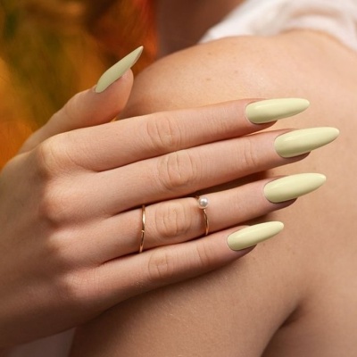 Mão feminina com unhas creme e anéis dourados sobre ombro de pele clara