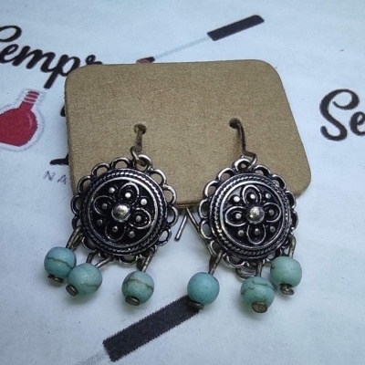 Brincos de metal com contas turquesa penduradas sobre cartão castanho