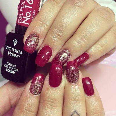 Frasco de verniz gel vermelho escuro Victoria Vynn e unhas pintadas com verniz vermelho escuro e glitter dourado