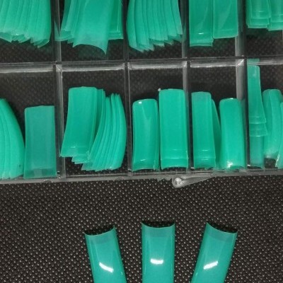 Caixa organizadora com unhas postiças verdes brilhantes de várias formas e tamanhos.