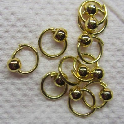 Argolas pequenas douradas com esfera, sobre fundo branco texturado