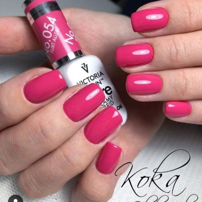 Unhas pintadas de verniz gel rosa forte segurando frasco branco de verniz VICTORIA VYNN.