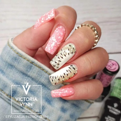 Unhas decoradas com verniz rosa com brilhos e detalhes dourados em fundo azul claro