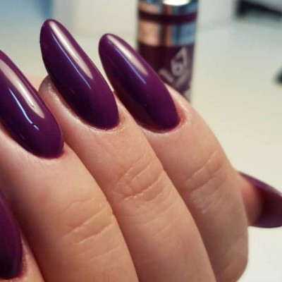 Unhas compridas em verniz roxo brilhante com fundo desfocado