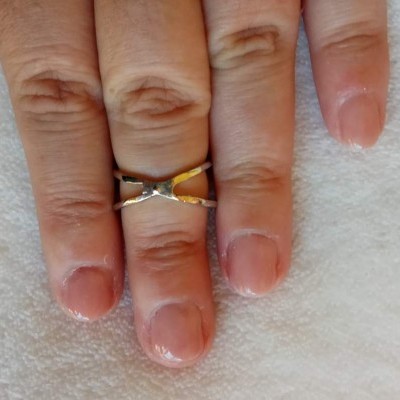 Mão com anel dourado entrelaçado no dedo médio sobre tecido branco