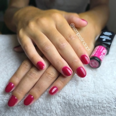 Mãos com unhas vermelhas sobre toalha branca com frasco de verniz cor de rosa