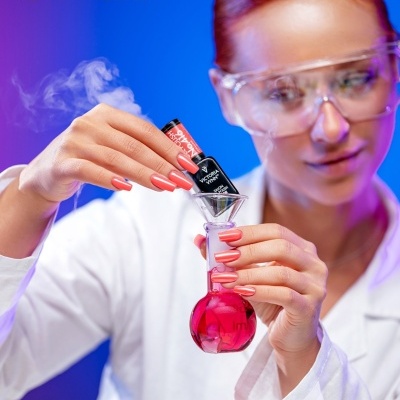 Mulher com bata e óculos a manipular verniz gel vermelho e preto em laboratório.