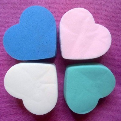 Quatro esponjas coloridas em forma de coração num fundo roxo