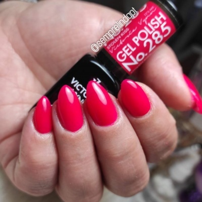 Unhas pintadas de verniz gel rosa vivo segurando frasco de verniz gel