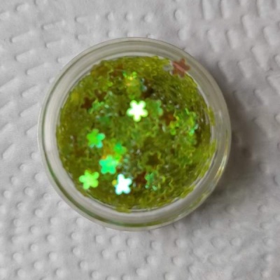 Frasco de glitter verde com partículas em forma de flores holográficas sobre fundo branco