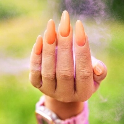 Mão com unhas longas pintadas de laranja sobre fundo verde desfocado