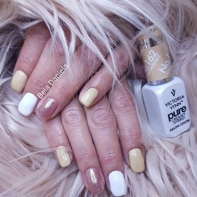 Mãos com unhas pintadas em bege, branco e glitter, com frasco de verniz dourado sobre pelo sintético claro