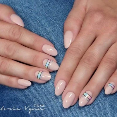 Mãos femininas com unhas pintadas de nude com linhas pretas e douradas, sobre jeans azul.
