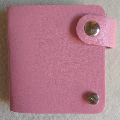 Carteira rosa quadrada com botão metálico prateado sobre fundo cinzento