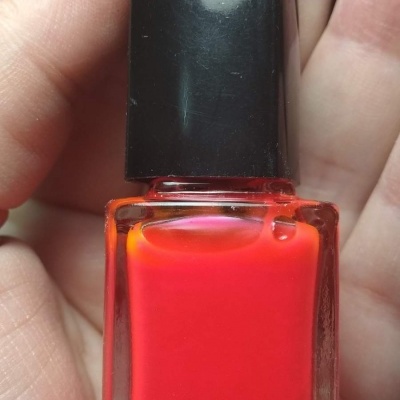 Frasco de verniz vermelho-alaranjado com tampa preta na mão