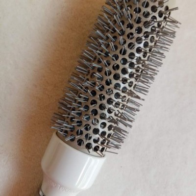 Escova redonda metálica para cabelo com pinos e cabo branco sobre superfície clara